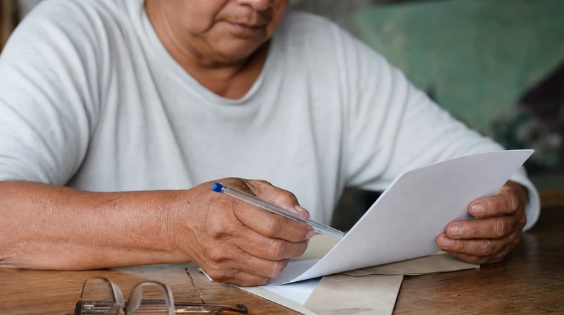 Manos de una persona mayor revisando sus documentos sobre la mesa